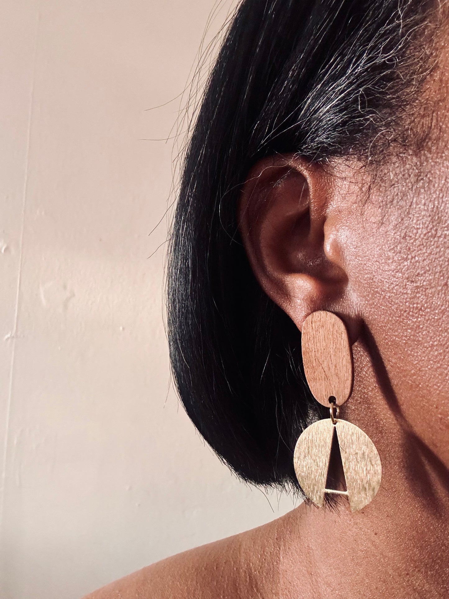 Close-up of an ear wearing a gold earring with a plain background
